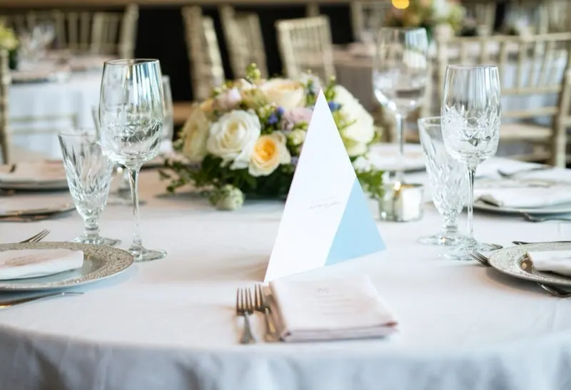 Tent card at the centre of a round gala dinner table with flowers and glassware